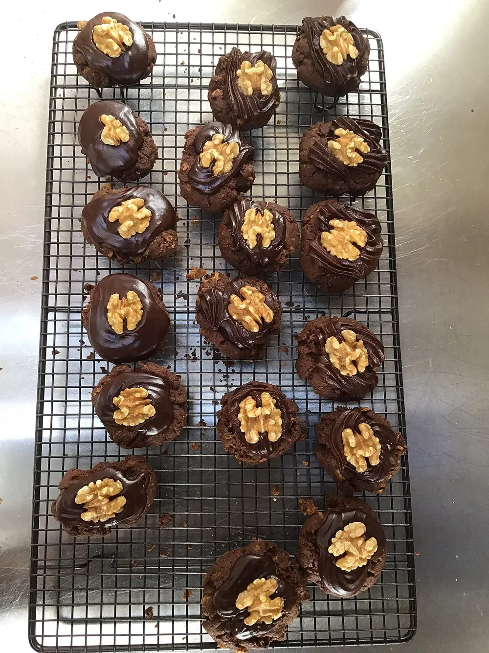 Afghan biscuits cooling on a wire rack, each iced with dark chocolate and topped with half a walnut