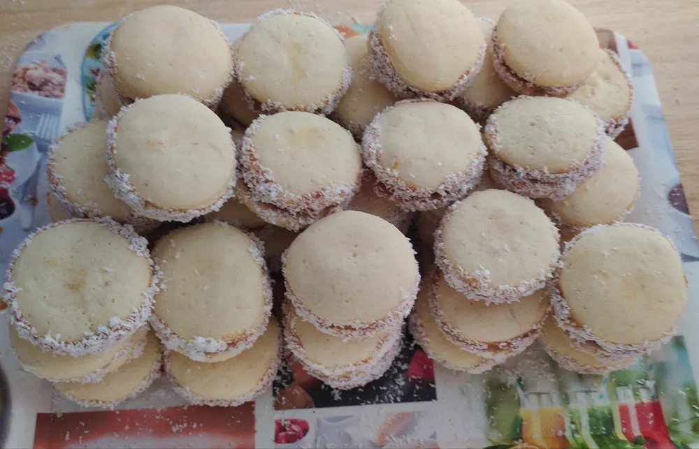 A tray of alfajores de maicena stacked up, each rolled edge-first in desiccated coconut