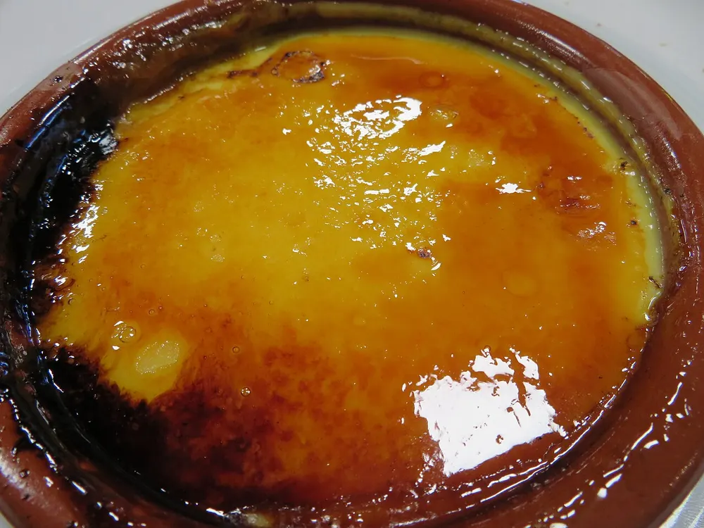 Crema catalana in a terracotta dish, its sugar top burnt to a glossy amber caramel.