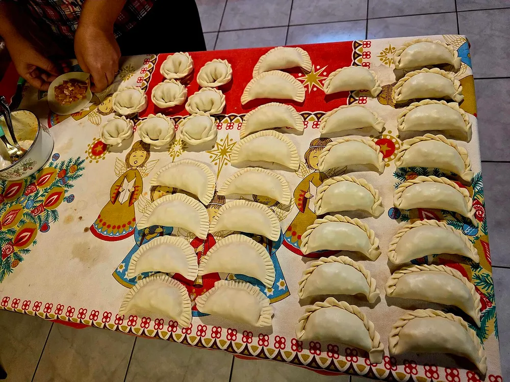 Trays of raw empanadas on a kitchen table, each row crimped with a different repulgue