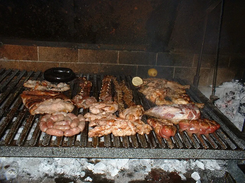 A full parrilla over embers — ribs, sausages, offal and a whole flank laid across the bars