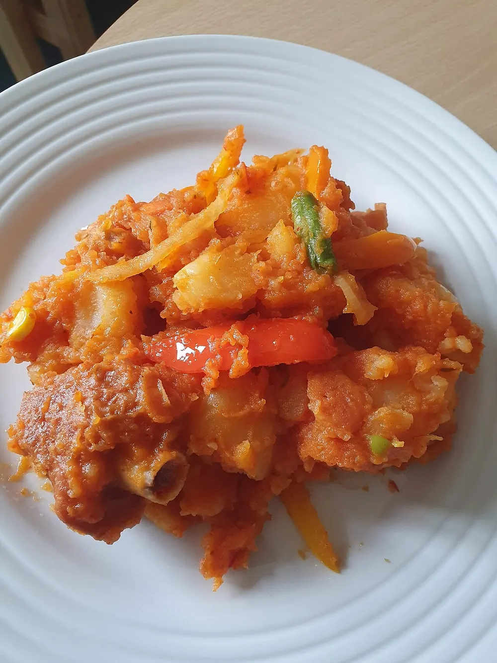 A plate of asaro — chunks of yam half-collapsed into a thick orange-red pepper sauce, with slivers of onion, strips of sweet pepper and a whole red chilli laid on top
