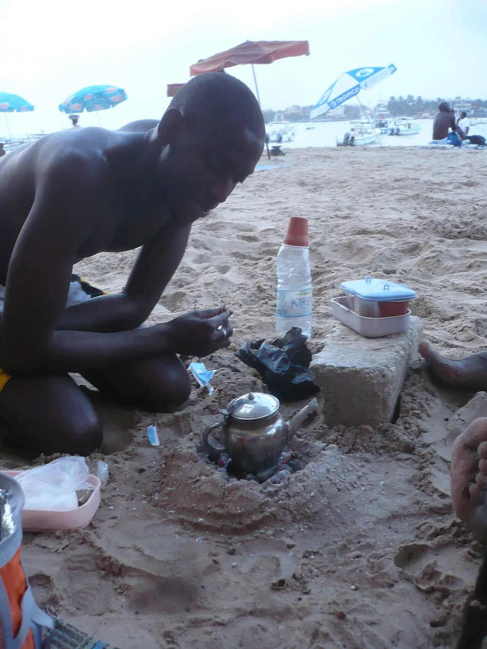 Attaya brewing in a small metal teapot over coals sunk into the sand on a Dakar beach