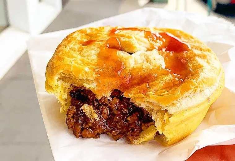 A golden Australian meat pie cut open to show the thick beef filling, topped with tomato sauce
