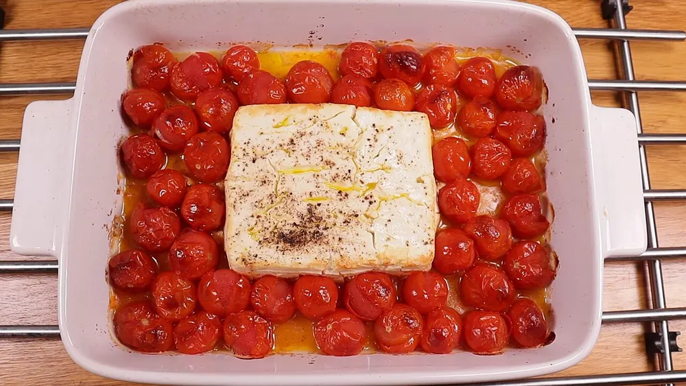 A whole block of feta baked among burst cherry tomatoes, photographed before the pasta is stirred through