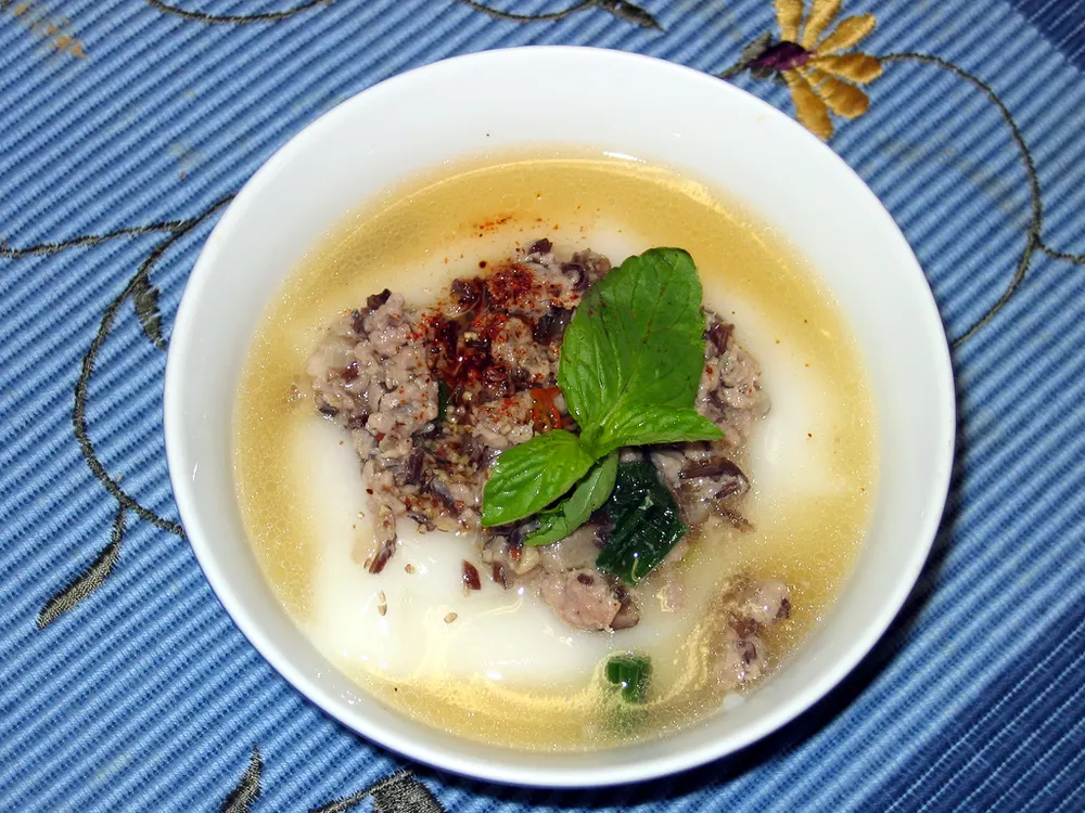 Bánh đúc nóng: hot northern rice cake in a bowl with pork and mushroom topping, herbs and chilli oil