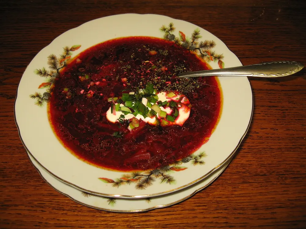 A bowl of deep ruby borscht topped with sour cream and chopped green herbs