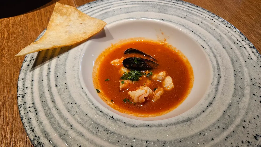 A plate of bouillabaisse — saffron-orange broth with white fish, a mussel and a prawn