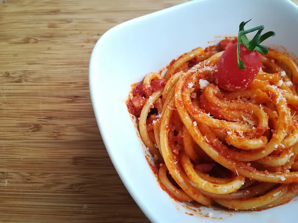 A bowl of bucatini all'amatriciana in a brick-red tomato sauce with grated pecorino