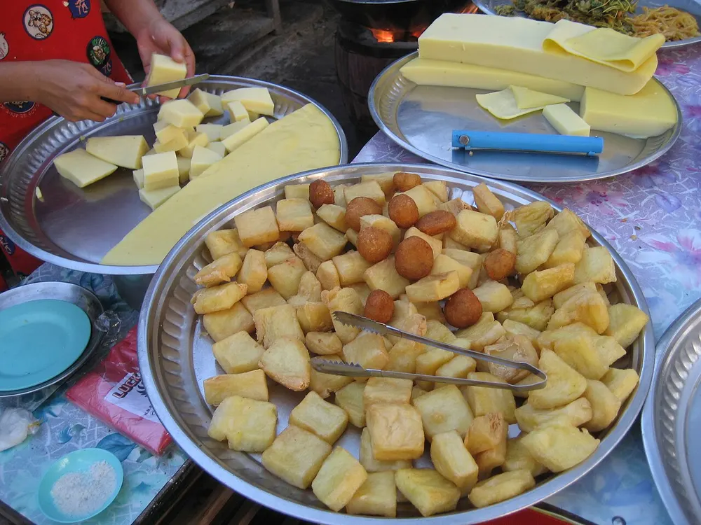 Slabs and fried cubes of Burmese chickpea tofu on a market tray