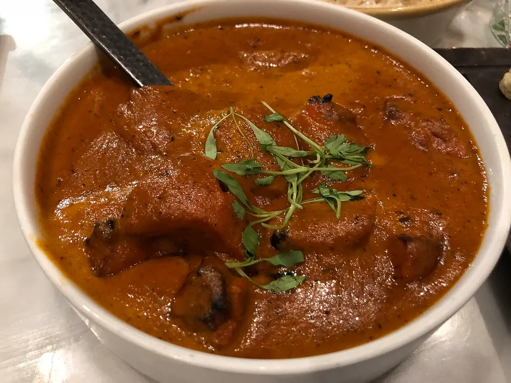 A bowl of butter chicken — charred chicken pieces in a creamy orange tomato sauce with fenugreek leaves
