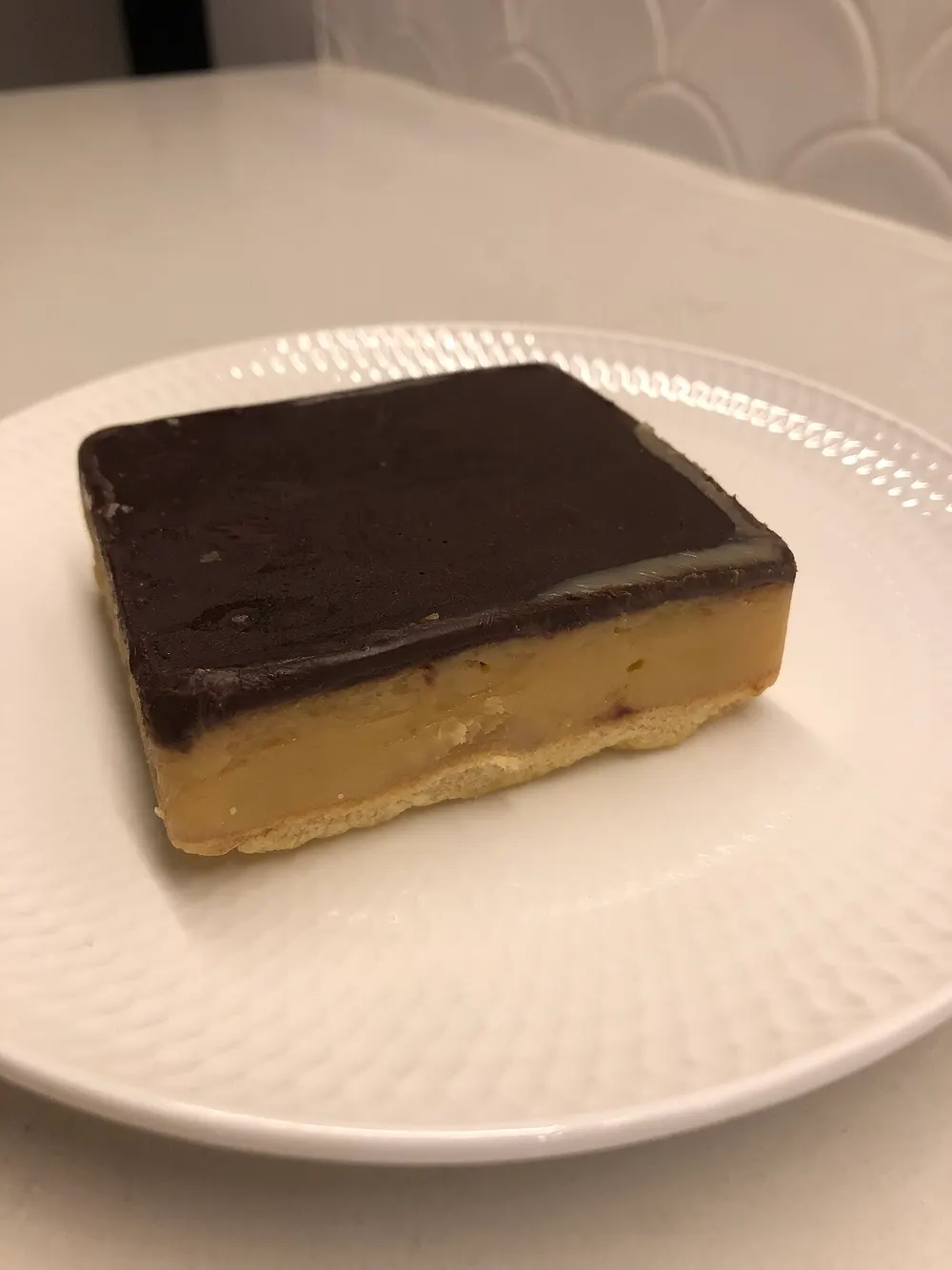 A square of caramel slice showing shortbread base, caramel middle and chocolate top