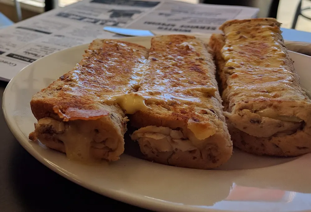 Three grilled cheese rolls on a plate in Otago, buttered and browned, the filling showing at the cut ends