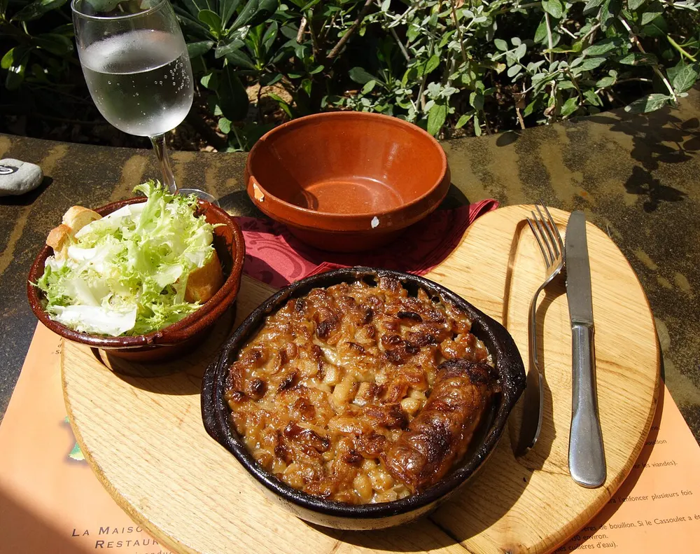 A cassoulet baked in a dark earthenware dish, its top browned and crusted, served with salad and bread
