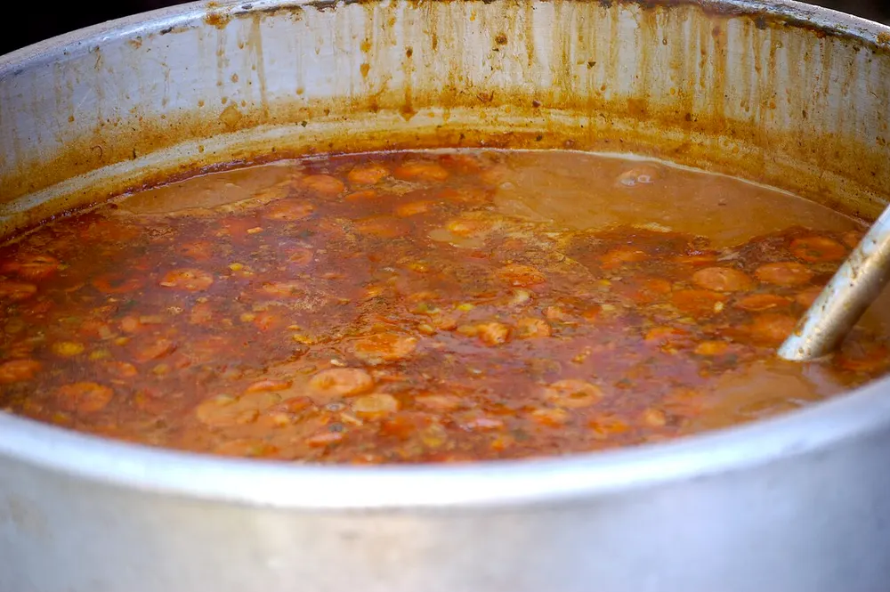 A large pot of dark reddish-brown gumbo with rounds of sausage visible throughout