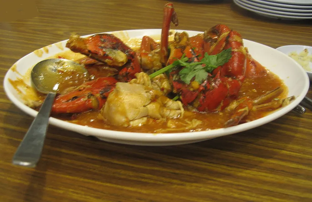 Pieces of whole crab in a thick red-orange chili gravy on a white platter, topped with cilantro