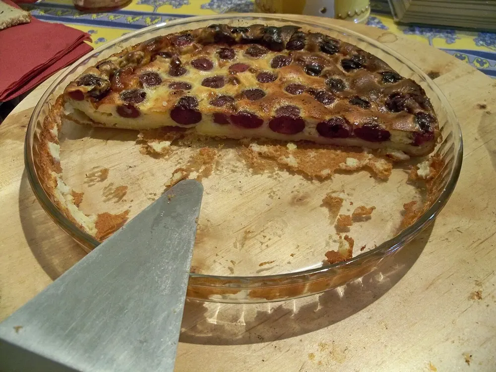 A cherry clafoutis in its baking dish with one slice lifted out