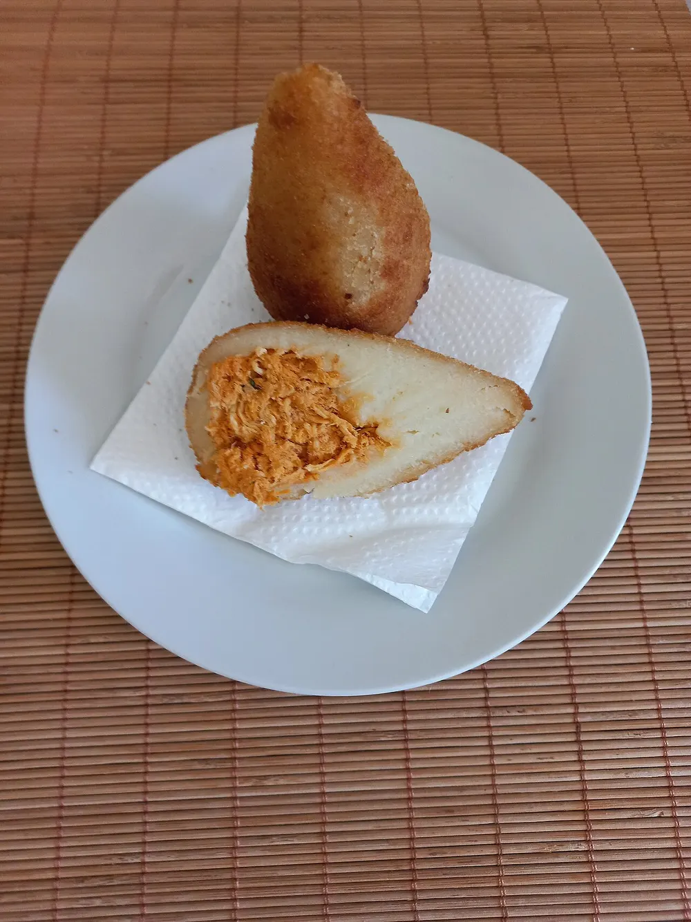 A whole teardrop coxinha and one cut open to show the shredded chicken filling