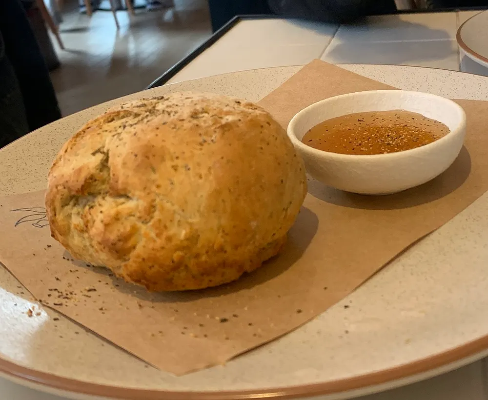 A round damper loaf on baking paper — a squat, unrisen soda-bread dome with a pale golden crust cracked open across the top, a small bowl of golden syrup beside it