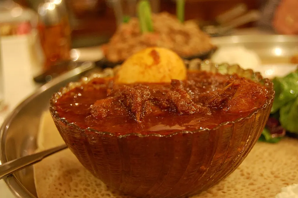 A bowl of deep red berbere stew with a whole hard-boiled egg, served on injera