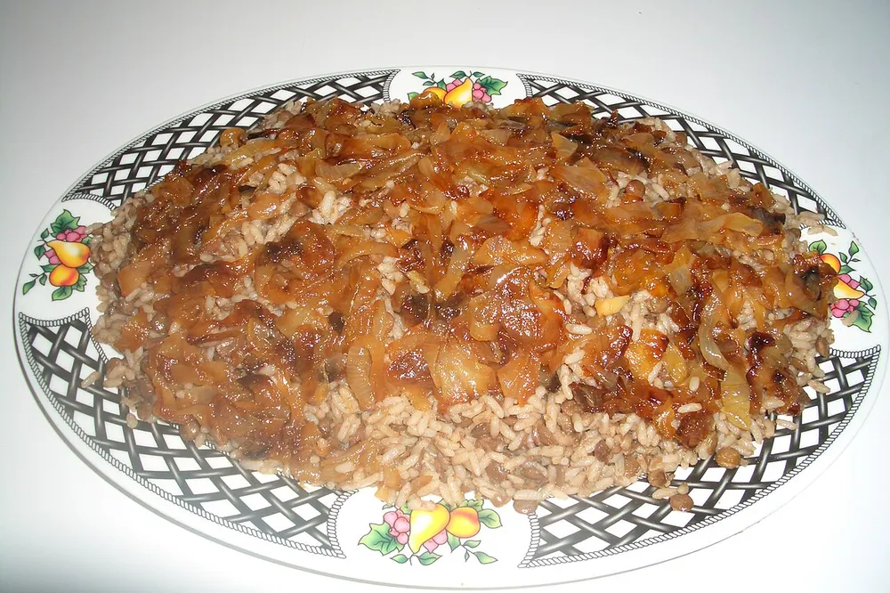 A serving platter of mujadara — lentils and rice mounded up and covered with a thick layer of deep-fried, dark golden onions