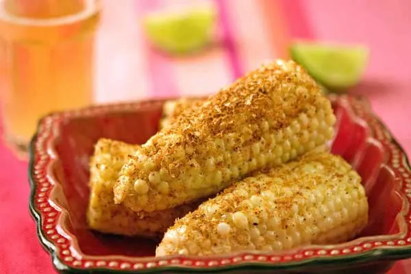 Corn on the cob dressed with crema and dusted with chili powder, with lime wedges