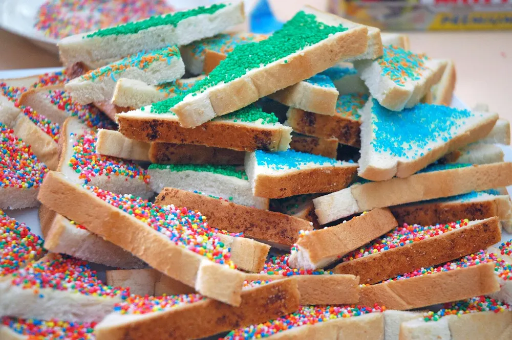 A pile of white bread fingers covered in colourful hundreds-and-thousands sprinkles