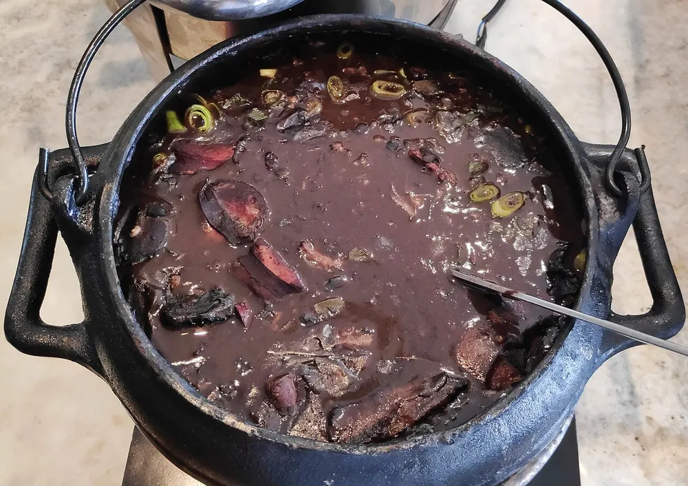 A cast-iron pot of black bean feijoada with sausage and pork cuts