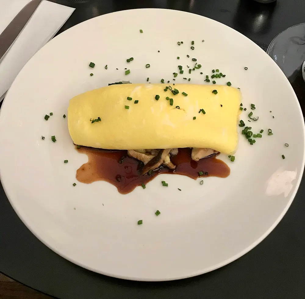 A French omelette rolled pale and unbrowned, served with mushrooms and herbs