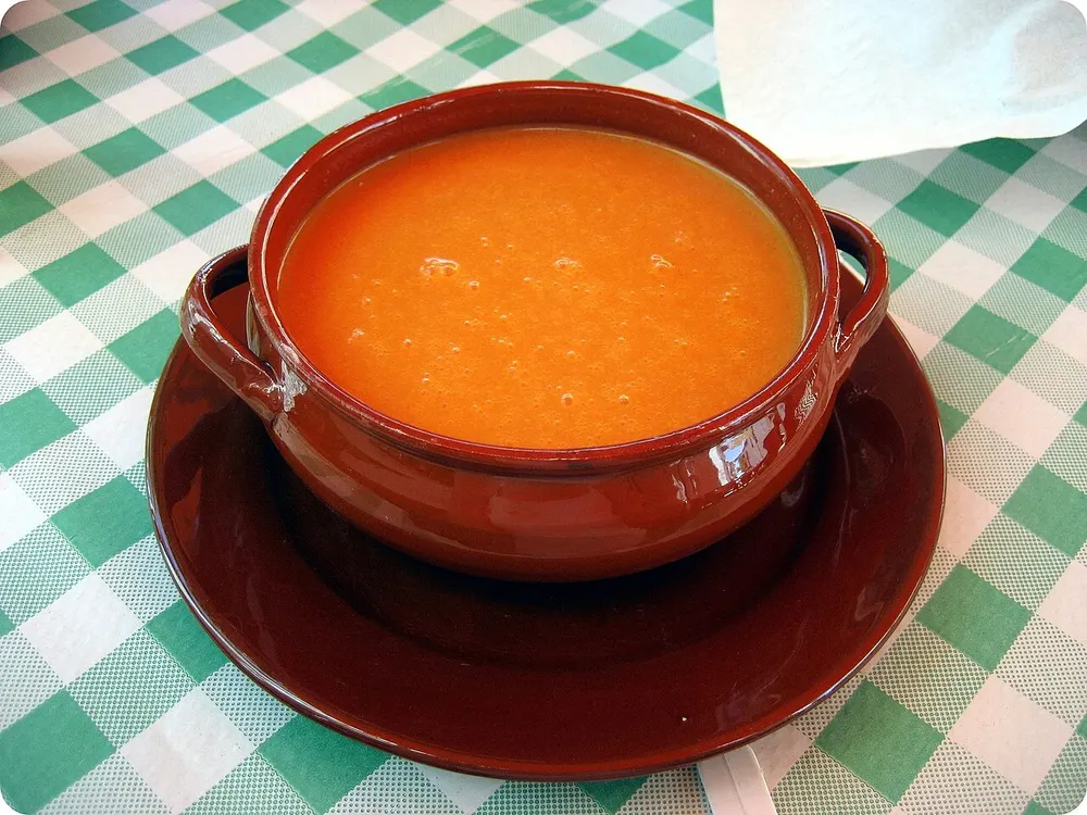 A terracotta bowl of smooth, chilled orange gazpacho
