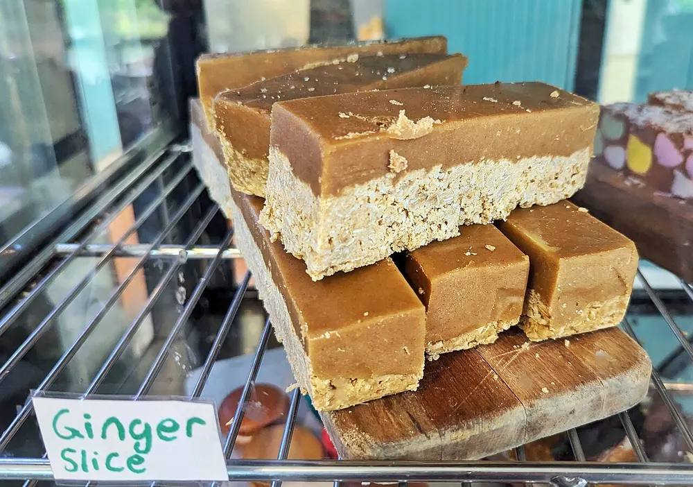 Slabs of ginger crunch stacked on a board in a Dunedin café, the thick ginger icing sitting on a pale crumbly base
