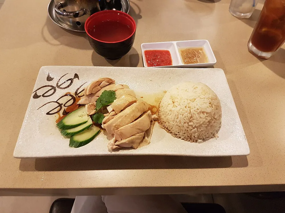 Sliced poached chicken with a dome of rice, cucumber, clear broth and chili and ginger sauces