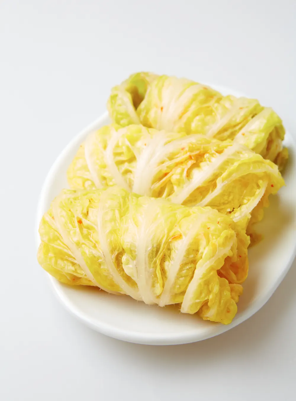 Three bo-kimchi parcels on a white dish, each bundled in a pale cabbage leaf