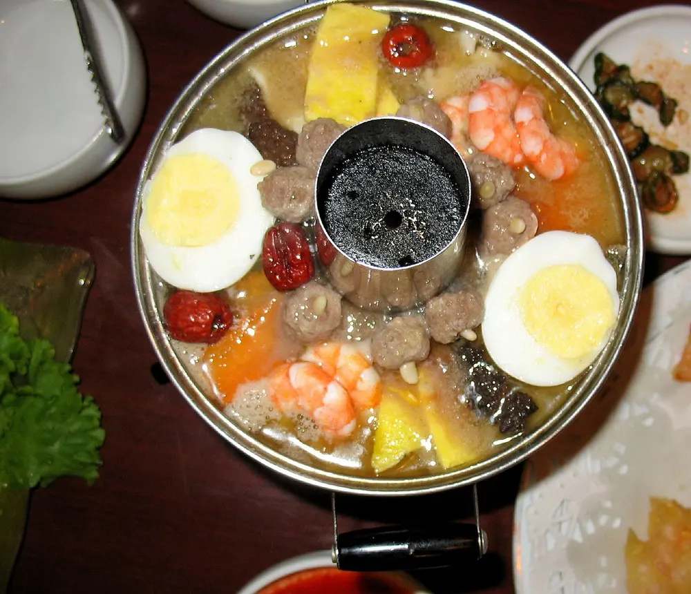 A brass sinseollo pot with its charcoal chimney, ringed with meatballs, egg, jujube and shrimp