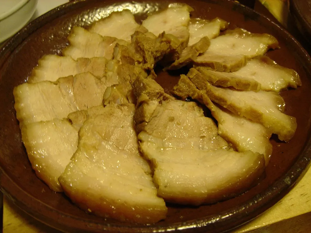 Suyuk — slices of boiled pork belly showing layers of fat and lean, arranged on a dark plate