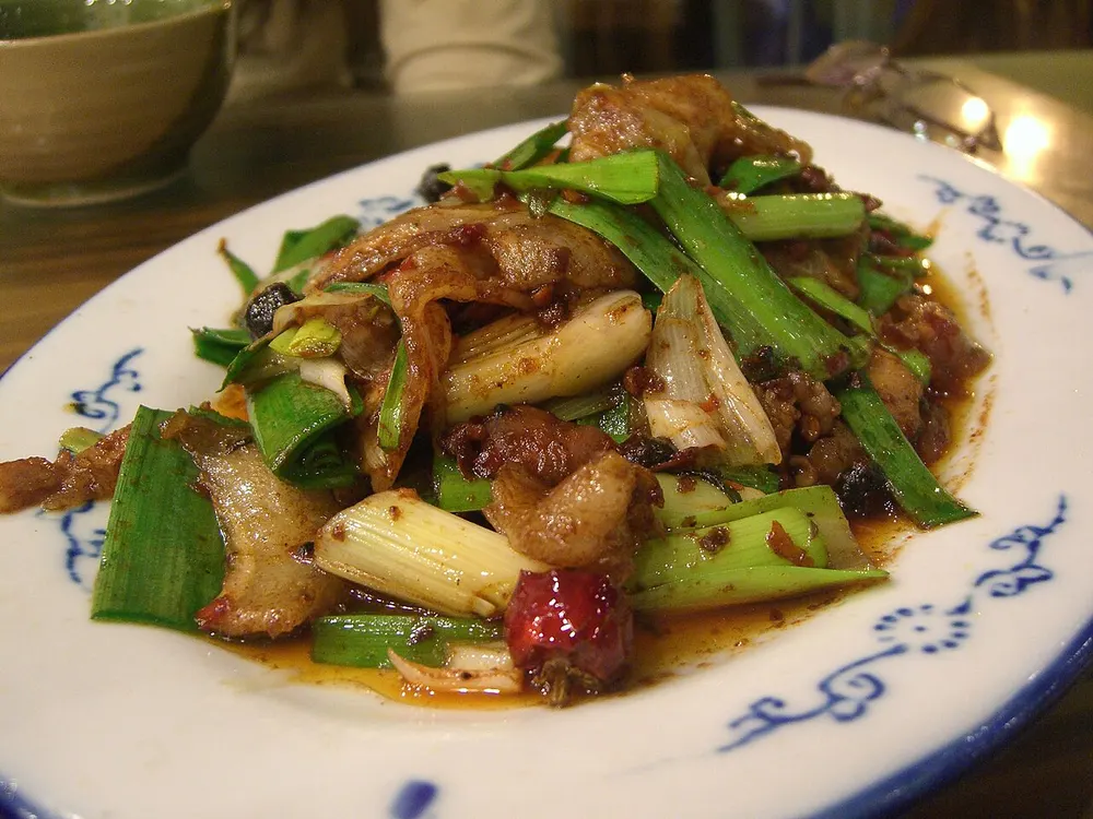 A plate of twice-cooked pork with curled belly slices and garlic sprouts