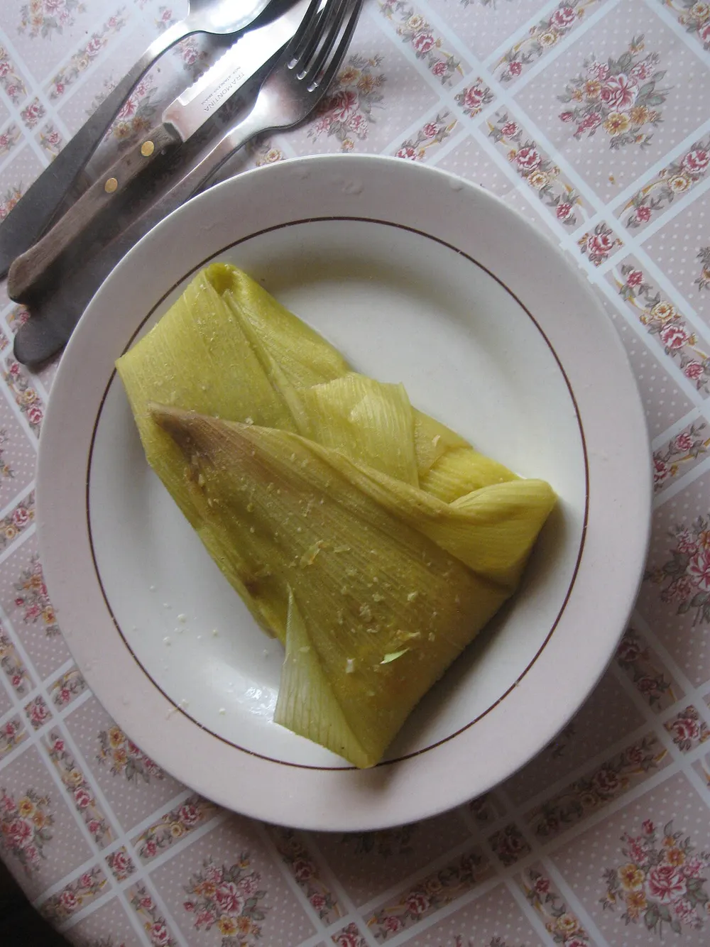 A humita on a plate, still tied in its corn husks