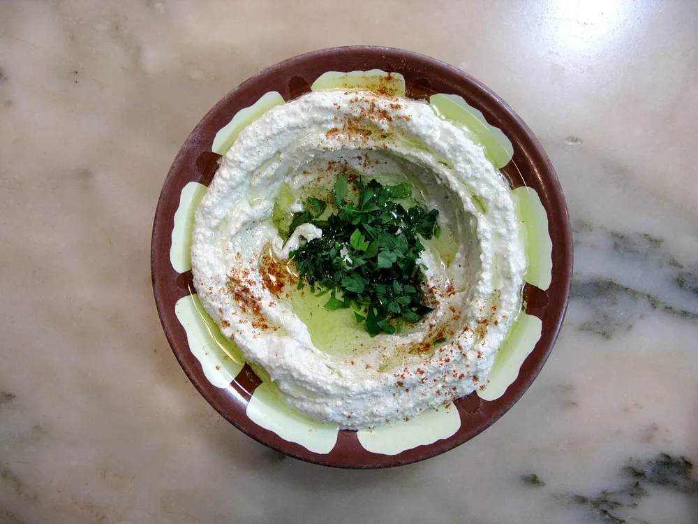A bowl of smooth hummus with olive oil pooled in the well, dusted with paprika and topped with parsley