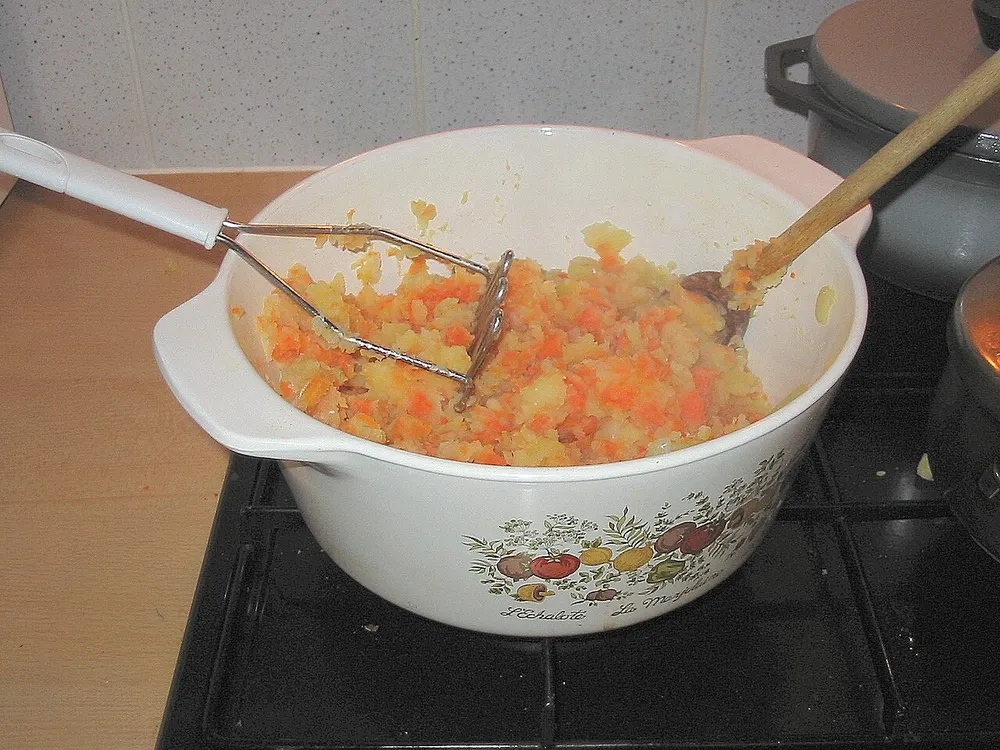 Hutspot being mashed in the pan — potato, carrot and onion still showing as separate colours