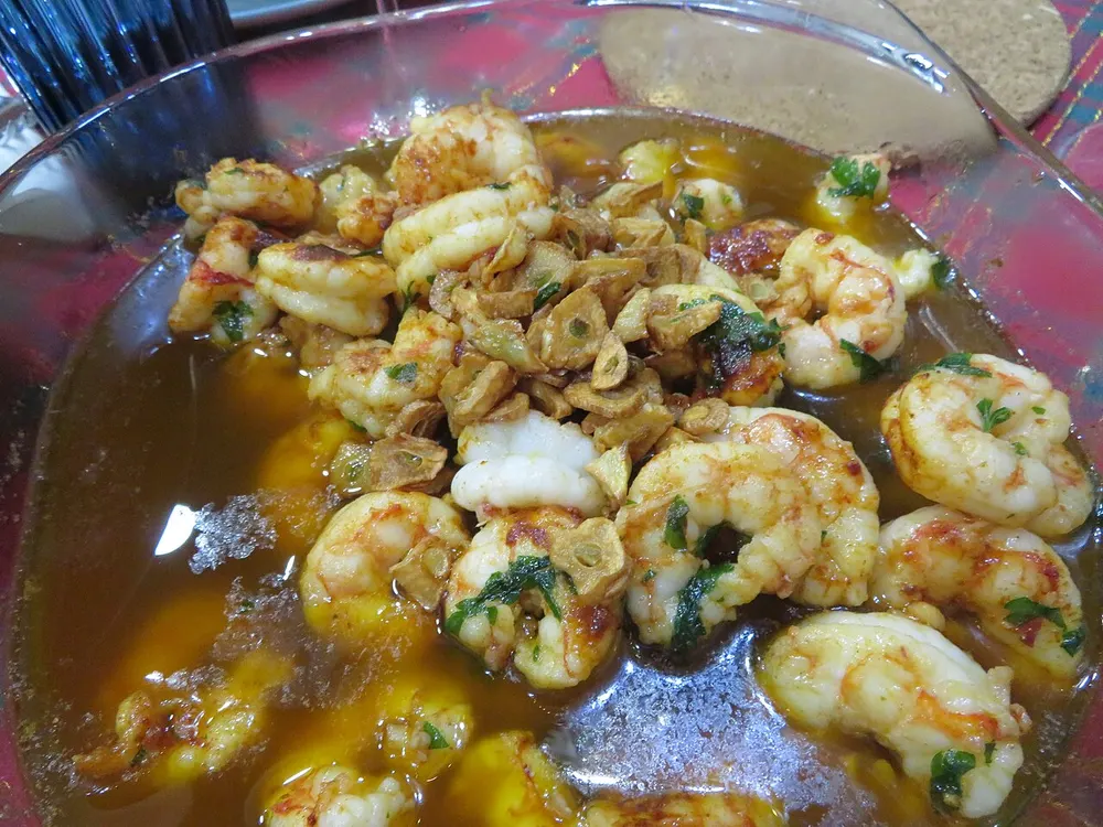 Gambas al ajillo in a shallow dish — pink prawns and thick slices of golden fried garlic in olive oil, flecked with chopped parsley