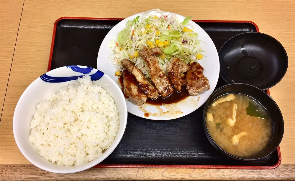 Tonteki — a thick pork steak sliced into fingers under a dark glossy sauce, served on shredded cabbage (photographed as a Japanese chain set meal, so rice and miso soup are also in frame)