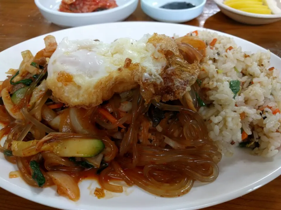 Japchae-bap — a red-sauced glass-noodle stir-fry with a crisp-edged fried egg on top, served with rice on the same plate (a Korean-Chinese restaurant serving, which also carries courgette and greens and serves the rice fried)