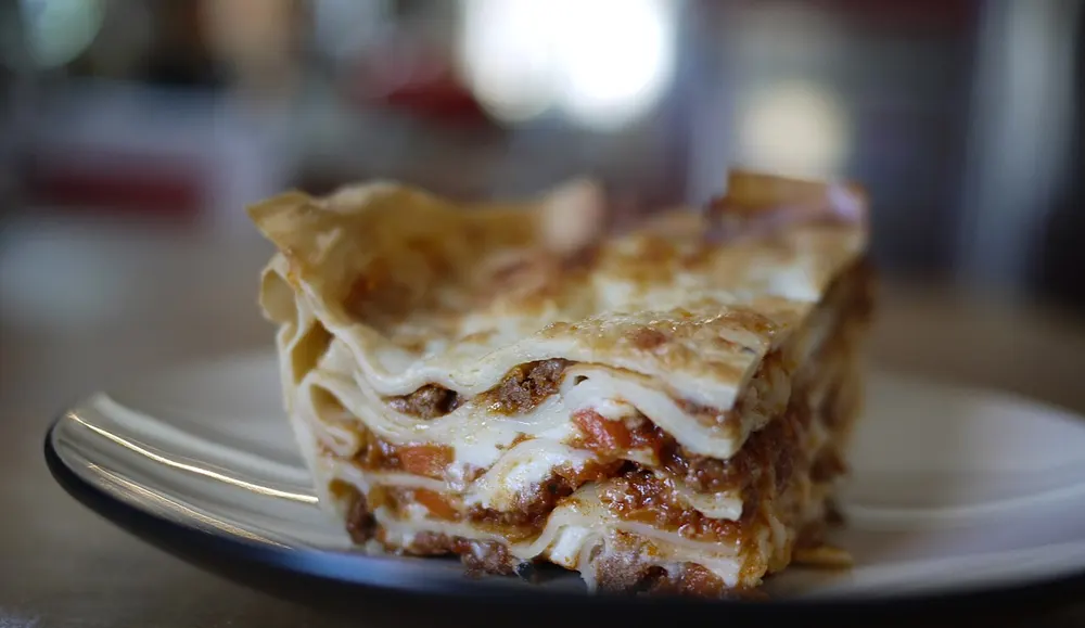 A slice of layered lasagne on a plate, showing pasta sheets, meat ragù and white sauce