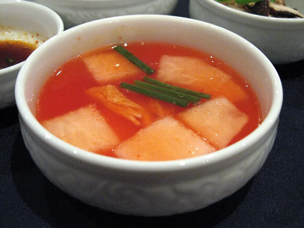 A bowl of nabak-kimchi — squares of radish and cabbage floating in a clear pink brine