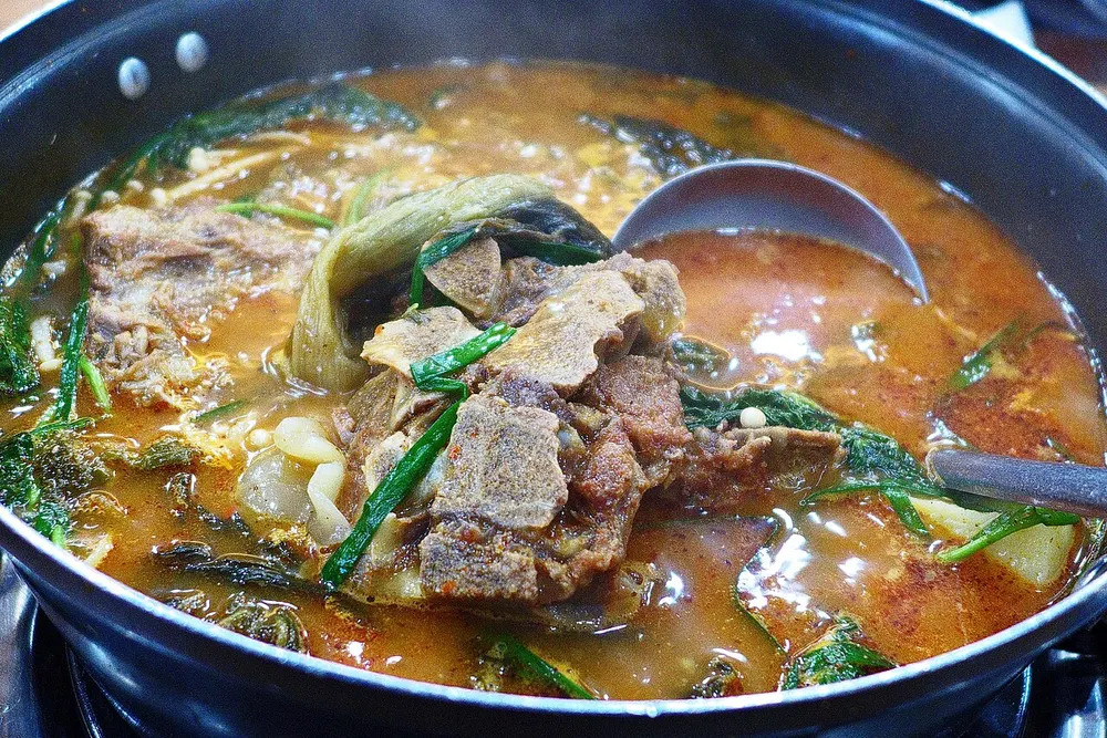 A bubbling pot of gamja-tang — pork back bones, potato and radish greens in a red broth