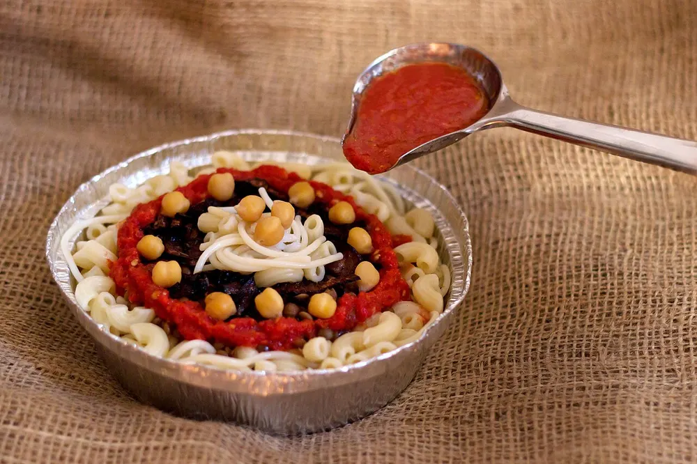A bowl of koshari — macaroni, vermicelli, lentils and chickpeas with tomato sauce and fried onions
