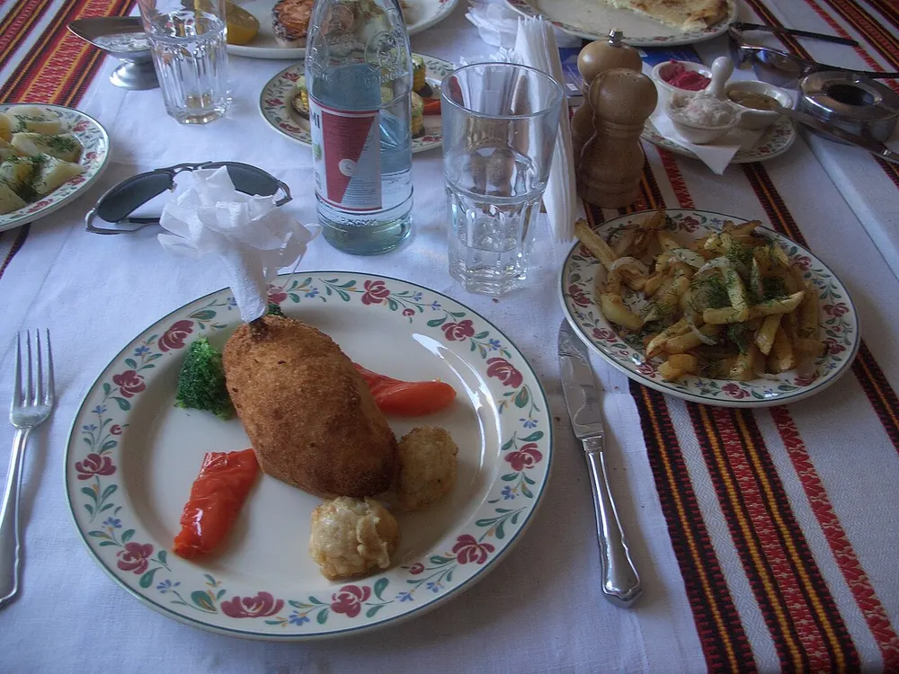 A chicken Kyiv cutlet with its paper frill, on a table laid with an embroidered runner