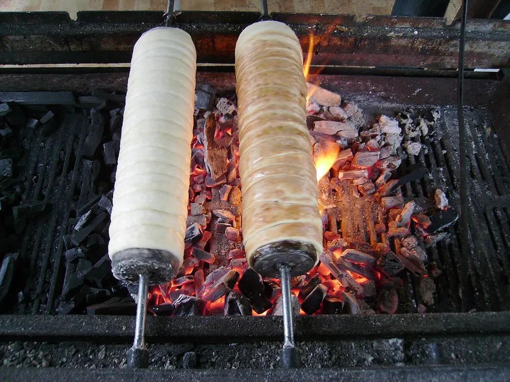 Two kürtőskalács turning on their spits over glowing charcoal