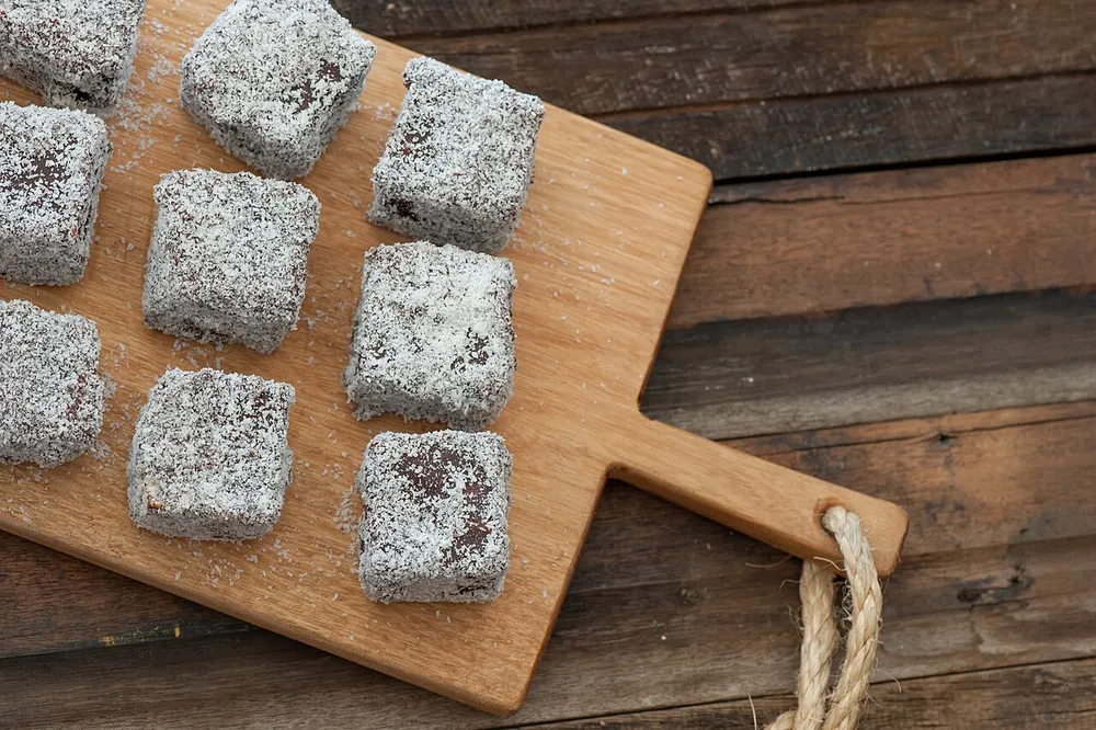 Coconut-coated chocolate lamington squares on a wooden board