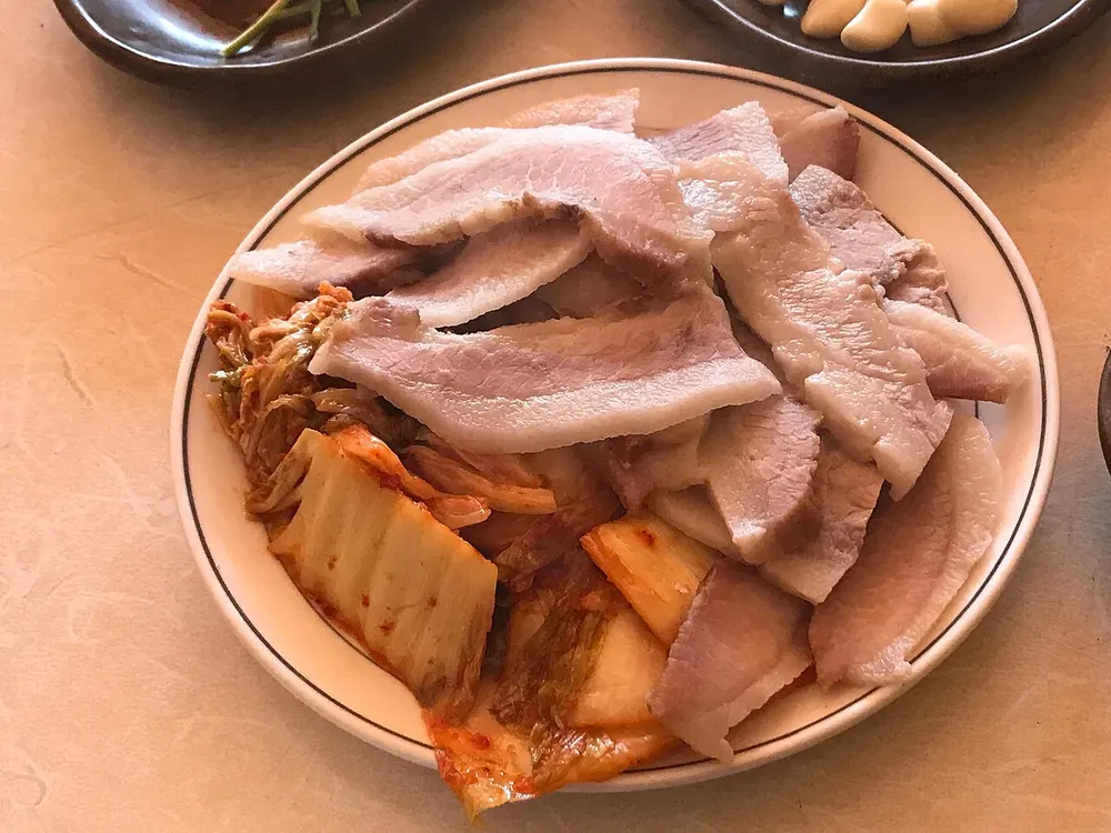 A plate of thinly sliced boiled pork belly served with kimchi